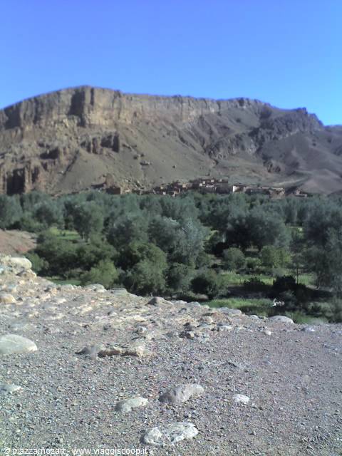Earthen village beneath rocky cliffs, olive groves in the green valley