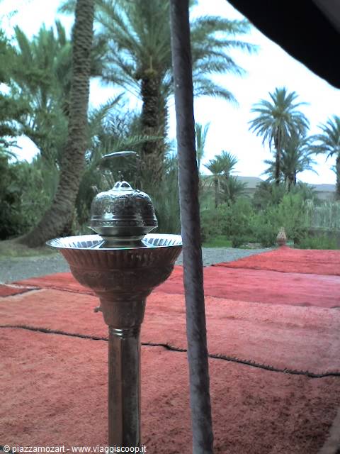 Silver teapot on a metal stand, red carpets and palm trees under a tent