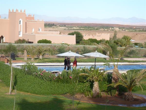 Tourists walk beside the pool of a kasbah-style resort, palms and mountains