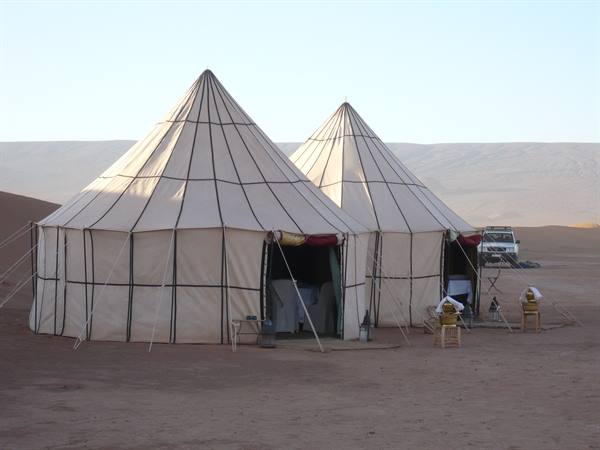 Two large canvas tents in the desert with jeep and tables, warm morning light