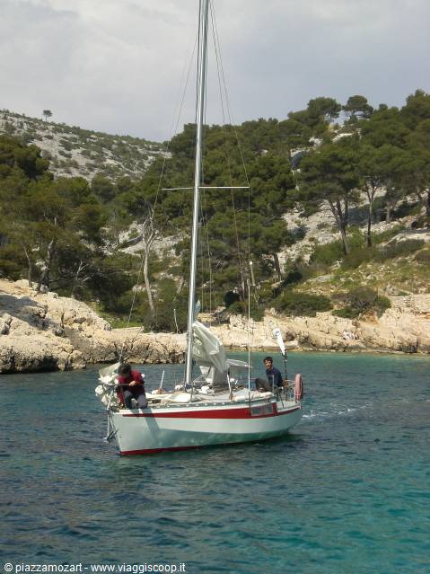 Two people on a white and red sailboat anchored in turquoise water