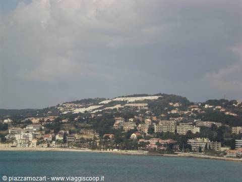 Coastal town with buildings and green hills under cloudy sky