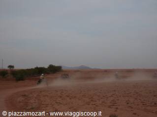 Motorbikes raise red dust on dirt track in desert