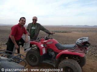 Two men next to a red quad bike in the rocky desert