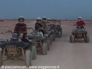 Kids wearing helmets riding quads in a line across the desert