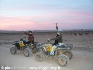 Two girls riding quad bikes in the desert arena at dusk, one waving