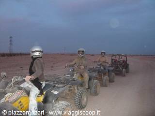 Group of helmeted tourists riding quad bikes on a dusty desert track