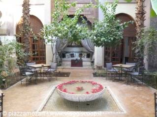 Courtyard with rose-petal fountain, palm trees and tables in a riad
