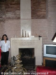 Woman beside an ornate carved stone fireplace, brick walls, old TV