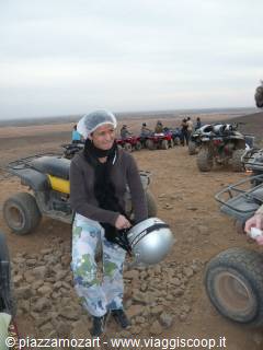 Tourist with helmet and bandana next to quad bikes on rocky desert