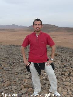 Man in red polo shirt and light trousers standing on desert stones
