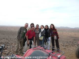 Group of tourists posing beside red quad bikes in rocky desert