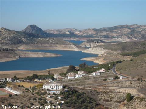 Blue lake between dry hills, white houses and an uphill road