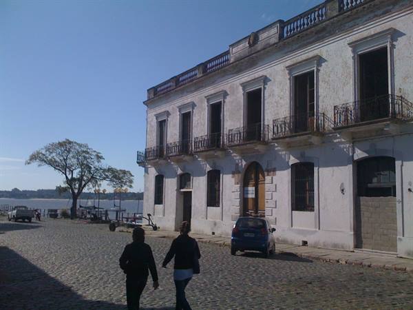 Women walk on cobblestones past an old white colonial building in Colonia del Sacramento