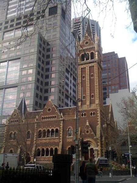Red brick Gothic church with tower among skyscrapers, Melbourne, pedestrians at traffic lights