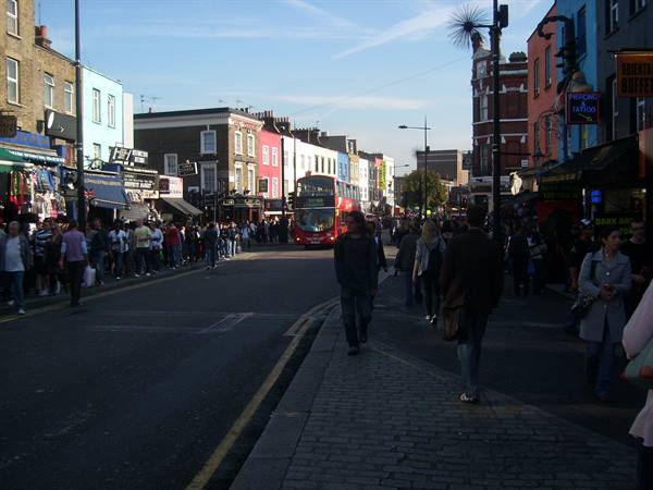 Crowds walking along Camden Town street, double-decker bus passing colorful shops