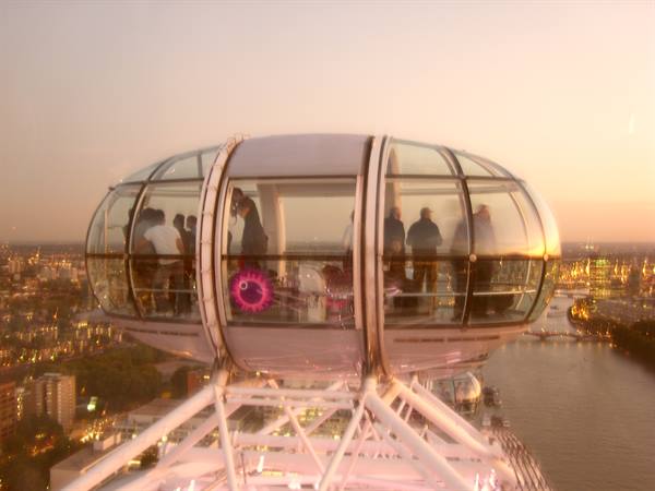 Glass capsule of the London Eye at dusk, tourists admiring the illuminated city