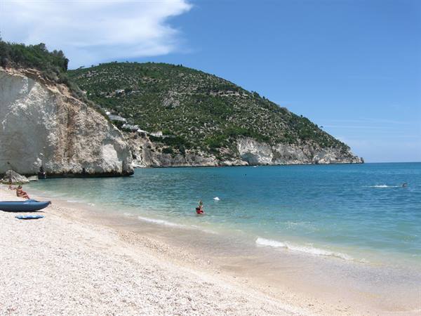 Pebble beach with white limestone cliff, blue kayak and swimmers in turquoise water