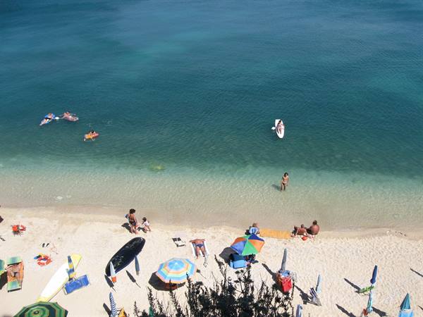 Sandy beach with colorful umbrellas, swimmers and canoes in turquoise water