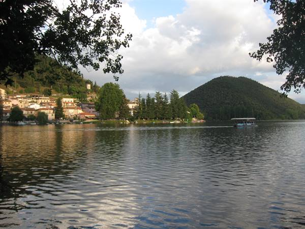 Boat crossing Lake Piediluco, village below wooded hills, cloudy evening light