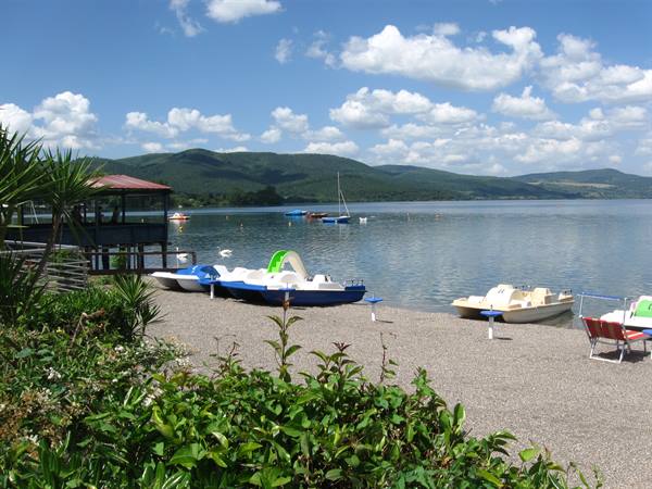 Pedal boats on the pebble beach, hills and clouds across the calm lake