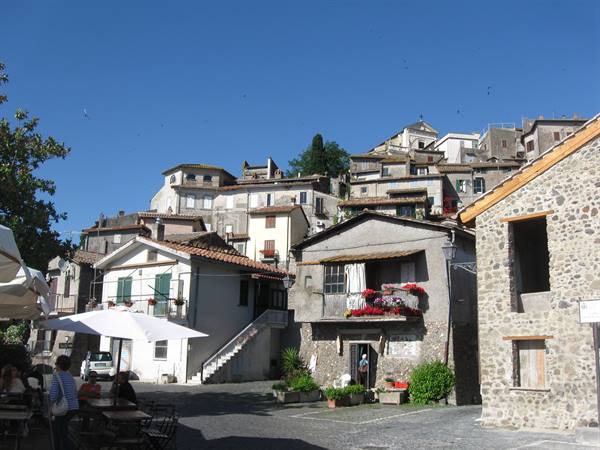 Small square with umbrellas beneath stone and brick houses of the hilltop village
