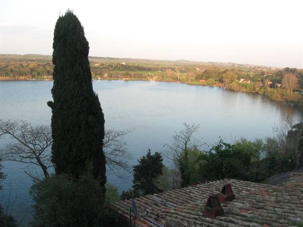 Cypress above tiled rooftops overlooking a lake ringed by green hills