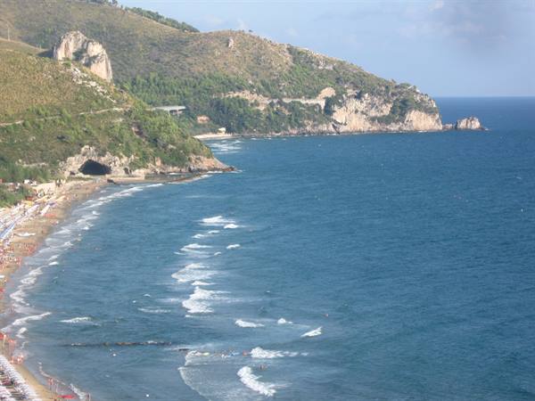 beach with umbrellas beneath green rocky hills and blue waves
