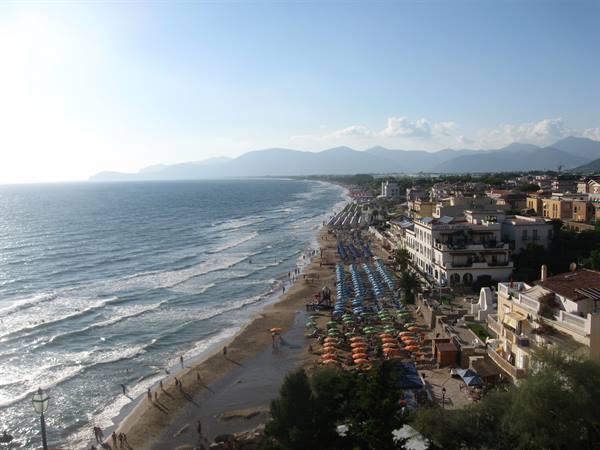 Beach with colorful umbrellas and swimmers, seaside hotels and mountains in the distance