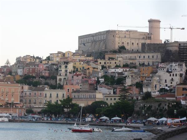 Aragonese castle above colorful hillside houses, boats moored at the waterfront below
