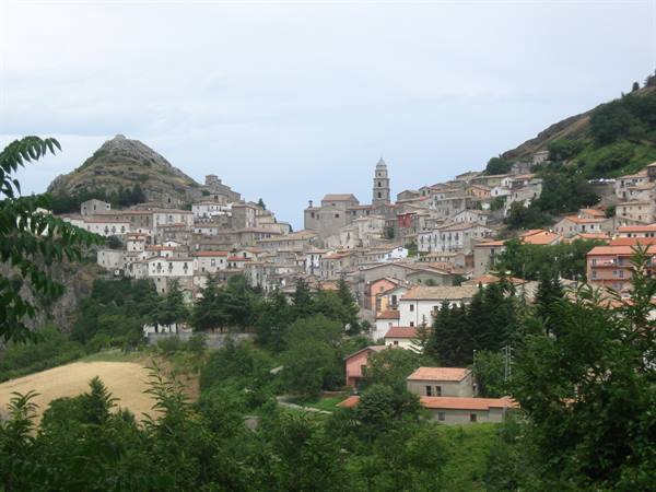 stone hillside village with bell tower among green mountains under gray sky