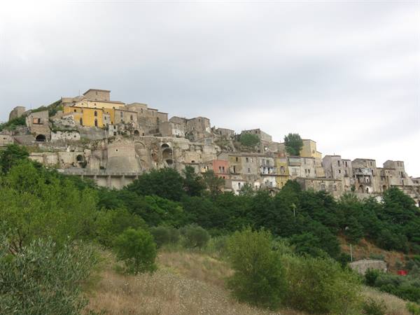 Abandoned stone village on a hillside above green trees and shrubs