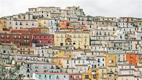 Hillside village of stacked colorful houses, ochre and pink facades under grey sky