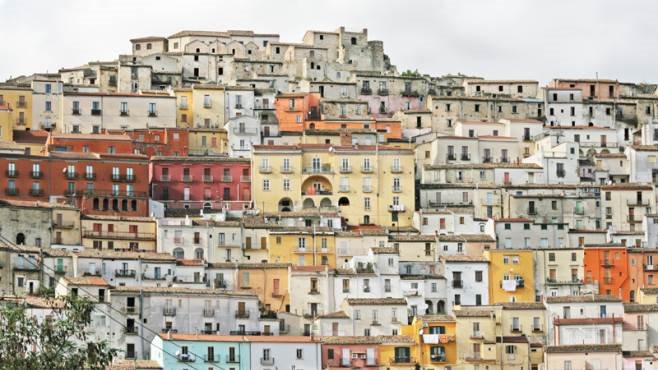 Borgo collinare con case colorate addensate, facciate ocra e rosa sotto cielo grigio