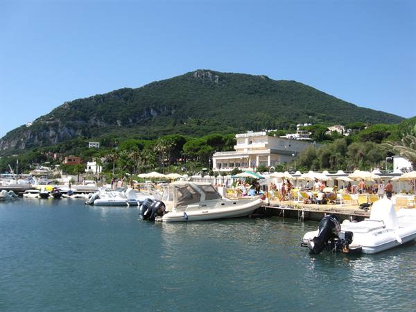 Motorboats moored at the marina below the green mountain, umbrellas along the shore