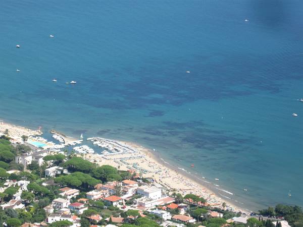 Marina with boats and sandy beach among houses, seen from above, turquoise sea