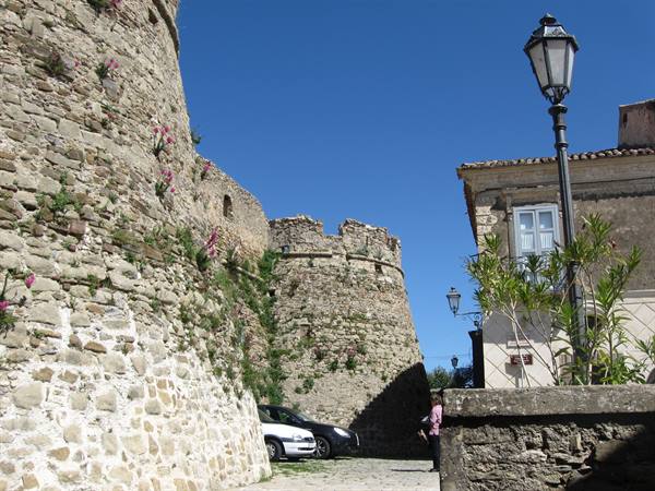 Aragonese castle walls in Vasto, stone towers, parked car beneath a clear blue sky