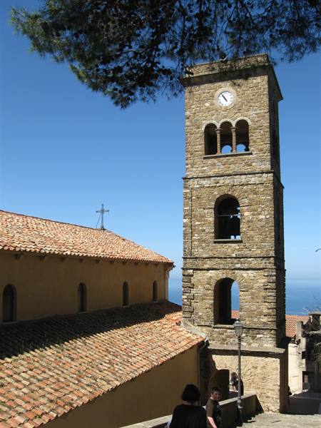 Stone bell tower with clock and tiled roofs above the sea