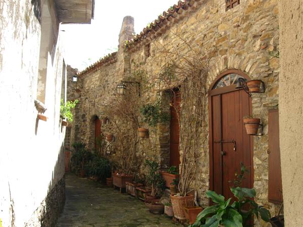 Alley with stone walls, wooden doors and potted plants in sunlight
