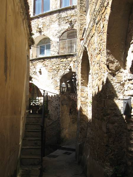 Stone alley with arches and staircase, sunlight between medieval houses