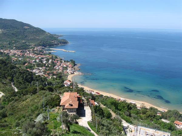 coastal village between green hills and sandy beach, turquoise sea under sunny sky