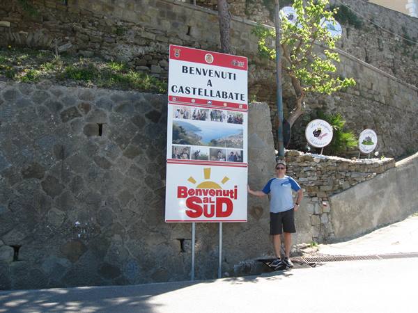 Tourist beside the Benvenuti a Castellabate sign on a stone wall