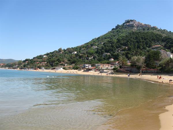 Sandy beach with clear water, bathers and sunny hilltop village