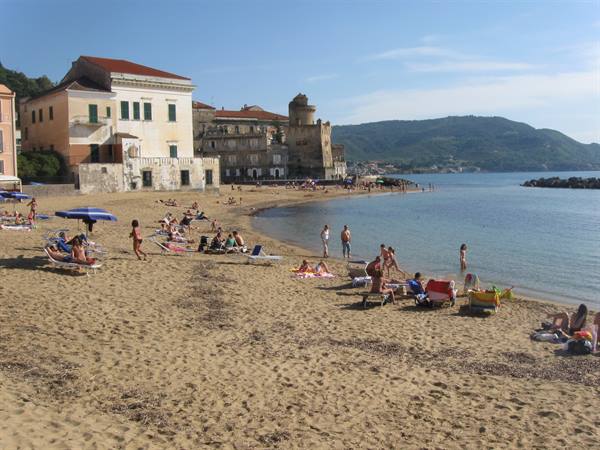 Sandy beach with sunbathers and umbrellas in front of old buildings and ancient tower at Santa Maria di Castellabate