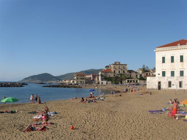 Bathers on sand in front of historic ochre buildings and calm sea