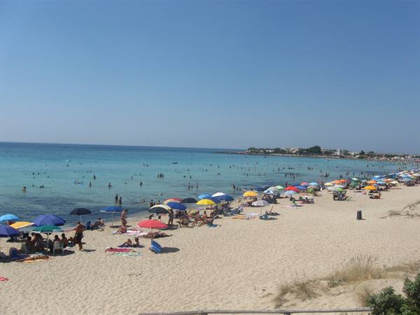 Crowded white-sand beach with colorful umbrellas and swimmers in turquoise water