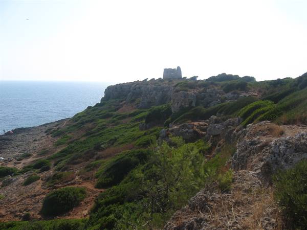 Ancient stone coastal tower on limestone cliff with Mediterranean shrubs above the sea