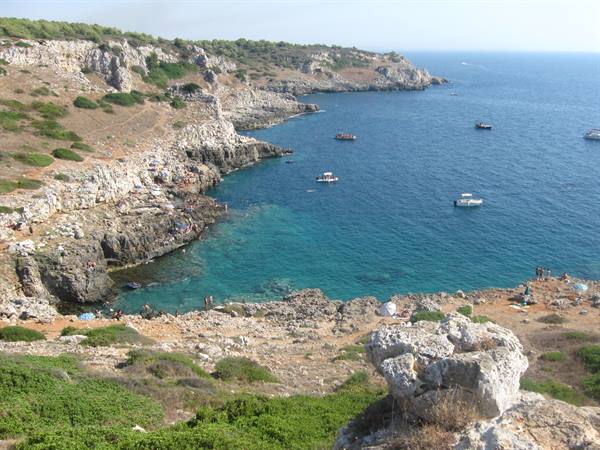 Rocky cove with turquoise water, boats offshore, limestone cliffs with swimmers