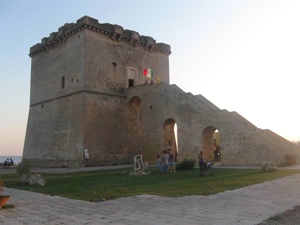 Tourists beneath the old coastal stone tower with Italian flag