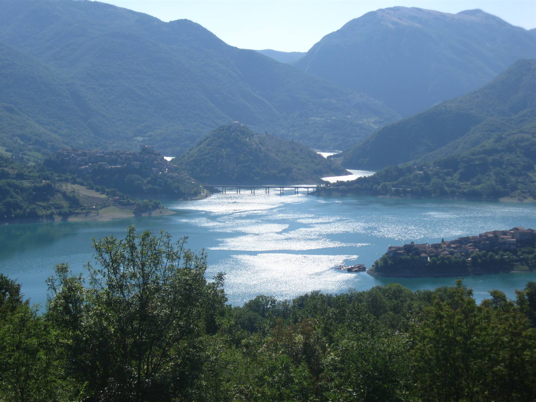 Ponte sul lago turchese tra monti e borgo, luce intensa